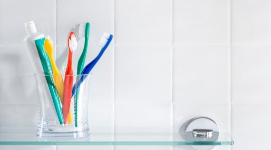 A clear glass on a shelf containing colourful toothbrushes