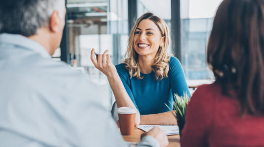 Woman smiling, sitting at table talking with others.