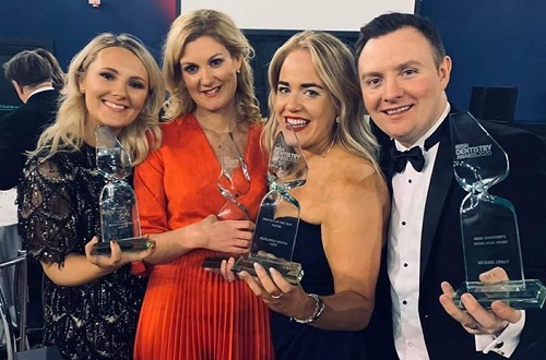 Photo of three women and one man at awards ceremony holding up awards and smiling