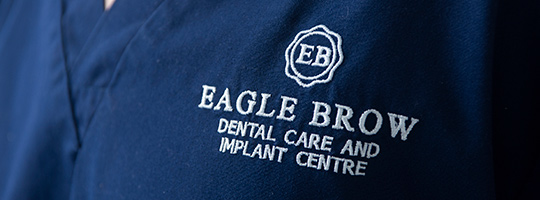 Eagle Brow logo and practice name embroidered in white thread on navy scrubs 