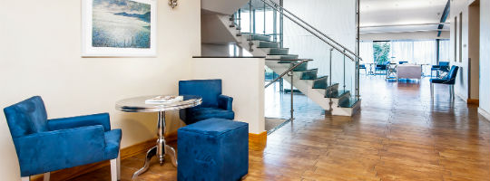 Photographic image of light and spacious dental practice waiting room with staircase and blue velvet armchairs