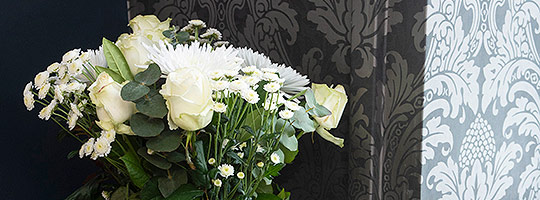 A bouquet of white flowers in front of blue filigree-patterned wallpaper