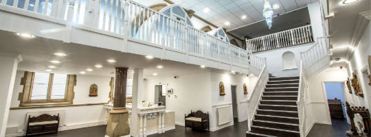 Photographic image of converted church with grand staircase, arched windows, chandelier and antique furniture