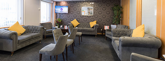 Photographic image of large dental practice waiting room with soft grey furniture and carpets, and yellow pillows and wall panelling