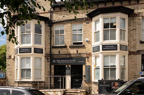 Photo of dental practice entrance. Grand building with bay windows and 'The Raglan Suite' sign above the door.