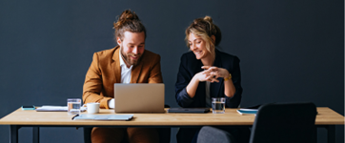 Office workers collaborating at desk using laptop in modern workspace, teamwork and productivity