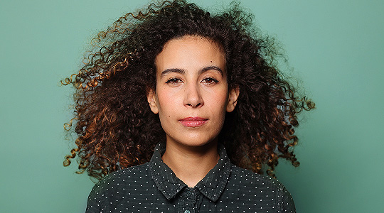 Portrait of person with curly hair against green background, studio headshot photography