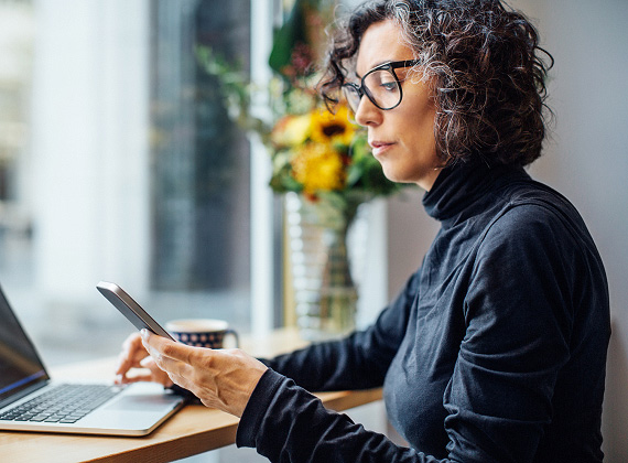 Person using smartphone at desk with laptop, showing mobile working and digital productivity