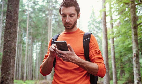 Man hiking through a forest and using his smartphone