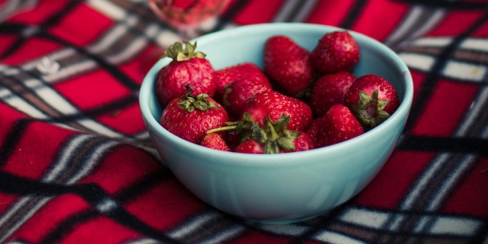 A bowl of strawberries on a picnic blanket