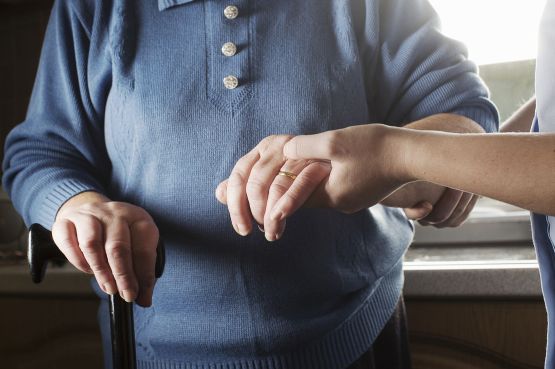 A carer helps an elderly lady with a walking stick