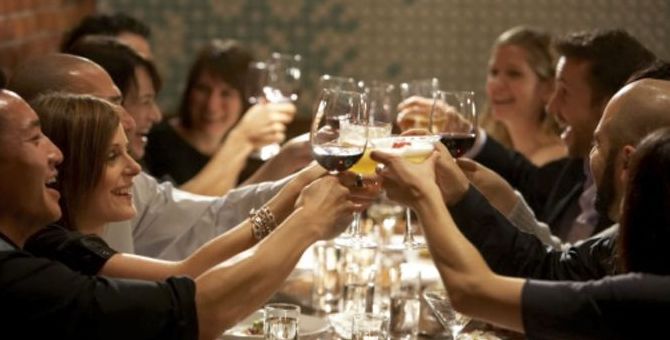 A group of friends clink their drinks over a dinner table